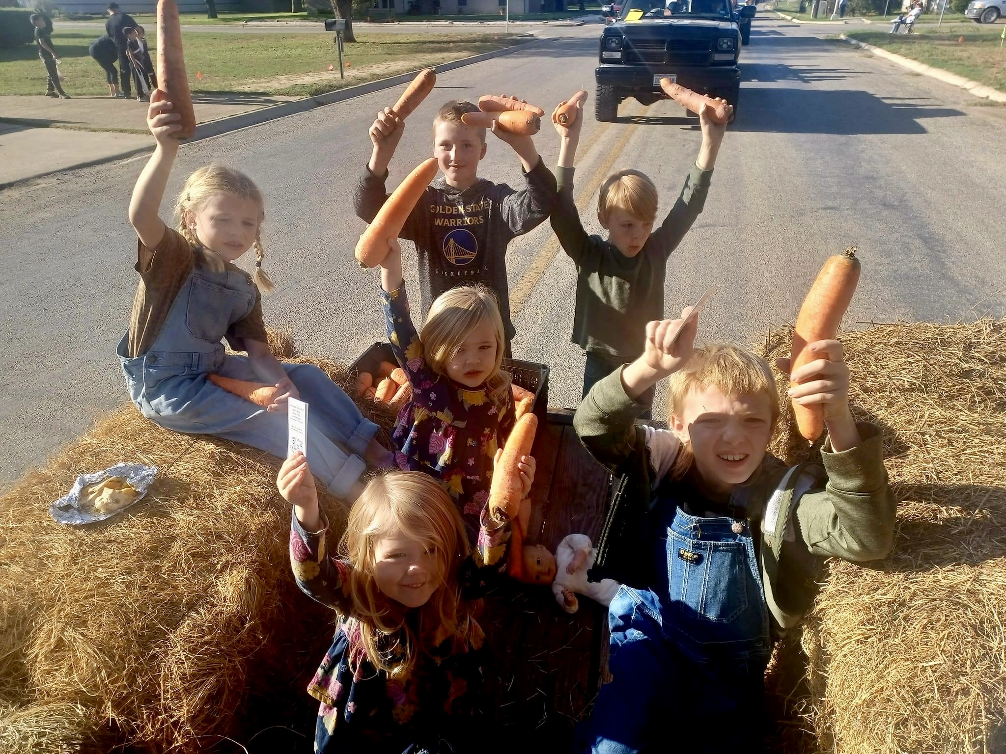 Kids on the Devine Market Association float holding up locally grown carrots.